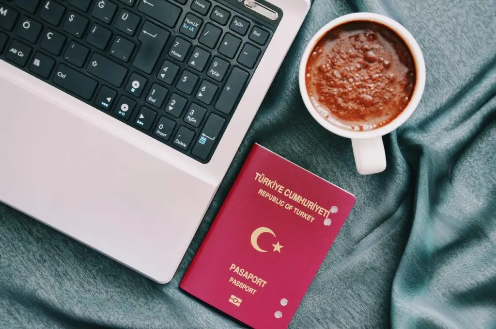 Turkish passport next to a cup of coffee and a laptop, symbolizing the process of obtaining Turkish citizenship through investment or naturalization.